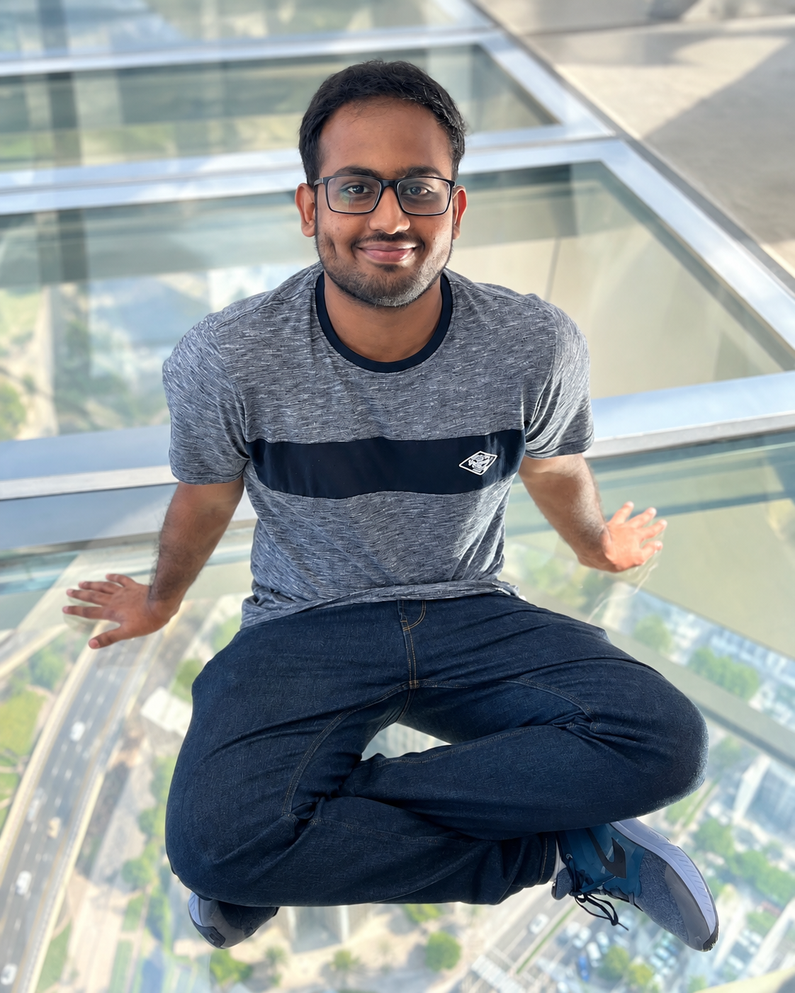 Bhavish Raj Gopal sitting on a glass-floor observation deck and smiling at the camera.